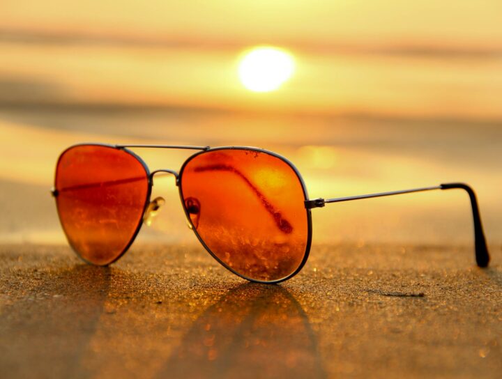 red lens sunglasses on sand near sea at sunset selective focus photography